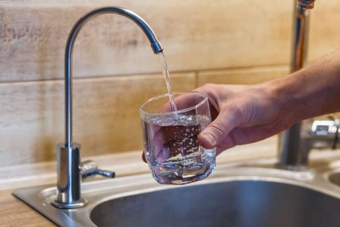 Man filling a glass of water from a dedicated drinking water spigot that's connected to a water softener / filtration system