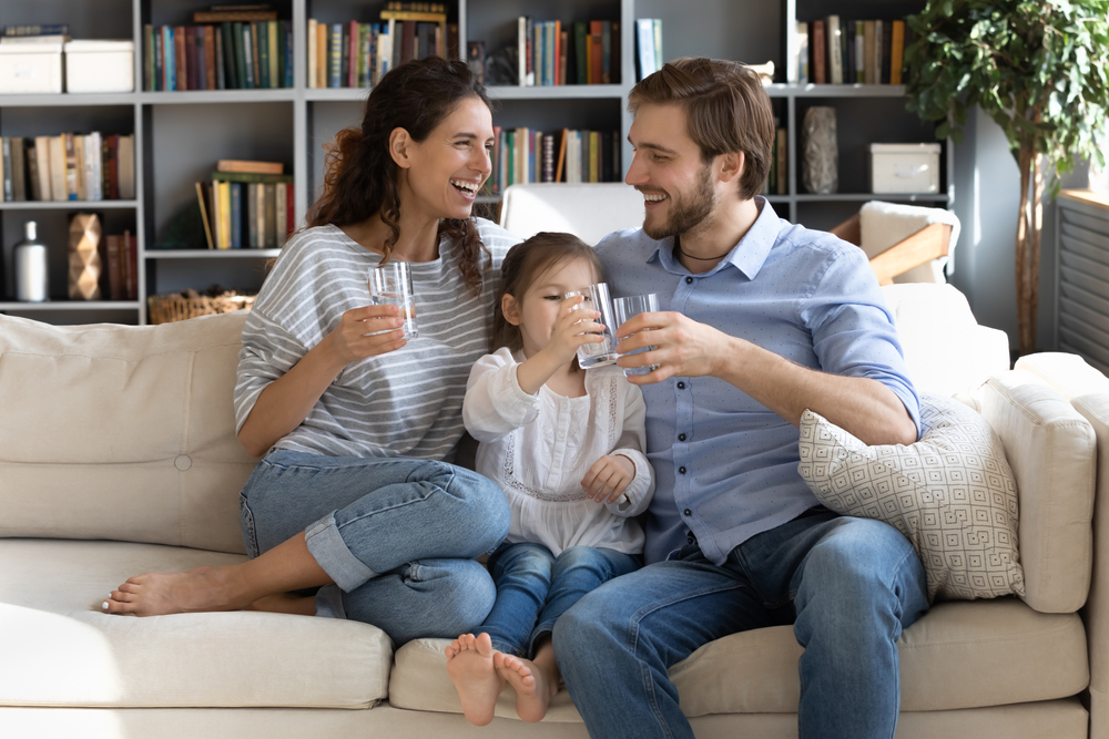 a mom and dad with their young daughter sitting on the couch and sipping glasses of filtered water
