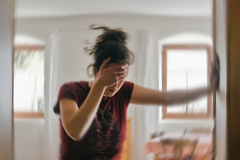 A blurred photo of a woman who feels dizzy and is holding her head and stabilizing herself on the wall