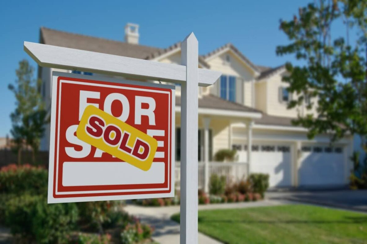 a For Sale sign on the lawn of a home with a Sold sticker placed over it
